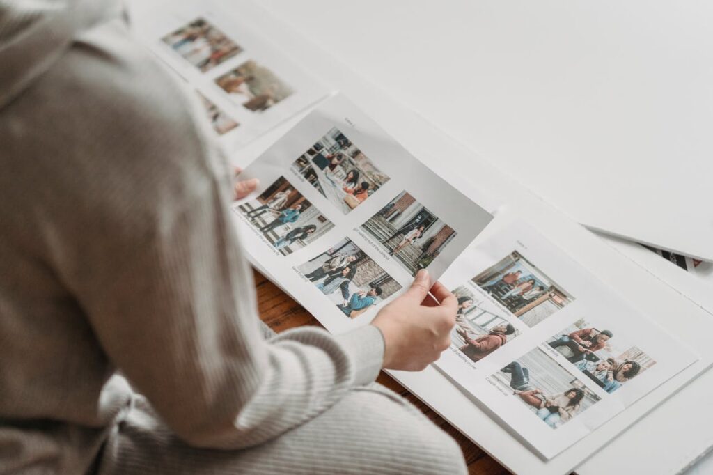 Individual in casual attire reviewing printed photo sheets indoors, capturing nostalgic moments.